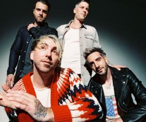 A photo of All Time Low, Alex Gaskarth is crouched at the front while all other members are standing behind him. 