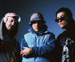 Ocean Grove photographed in front of a blue backdrop, they are all wearing casual attire and Dale is wearing a bucket hat. 
