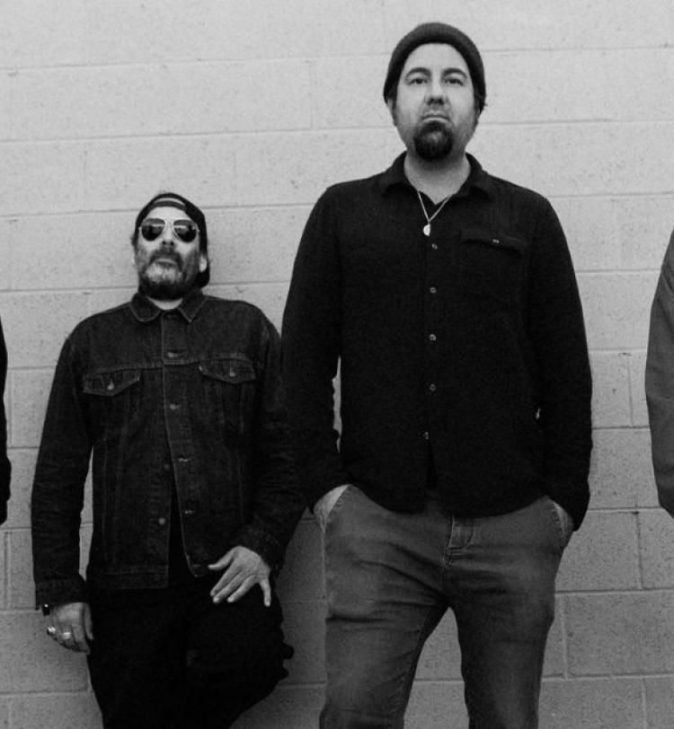 A black and white photo of Deftones standing against a white wall, all members are wearing casual clothes