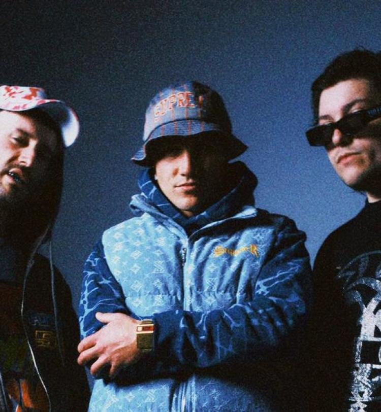 Ocean Grove photographed in front of a blue backdrop, they are all wearing casual attire and Dale is wearing a bucket hat. 